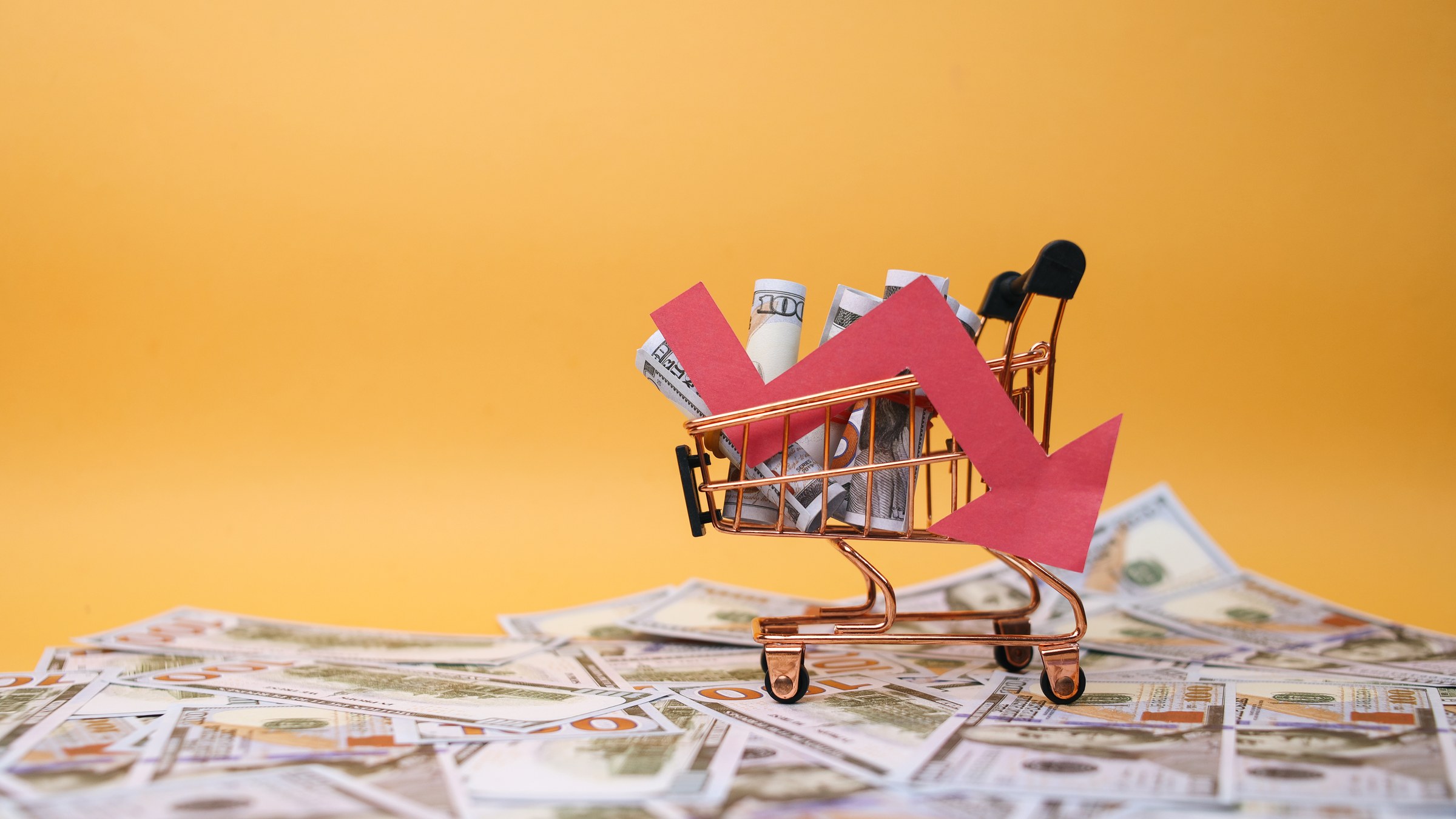 Miniature shopping cart on currency with a declining arrow, marketplace fees