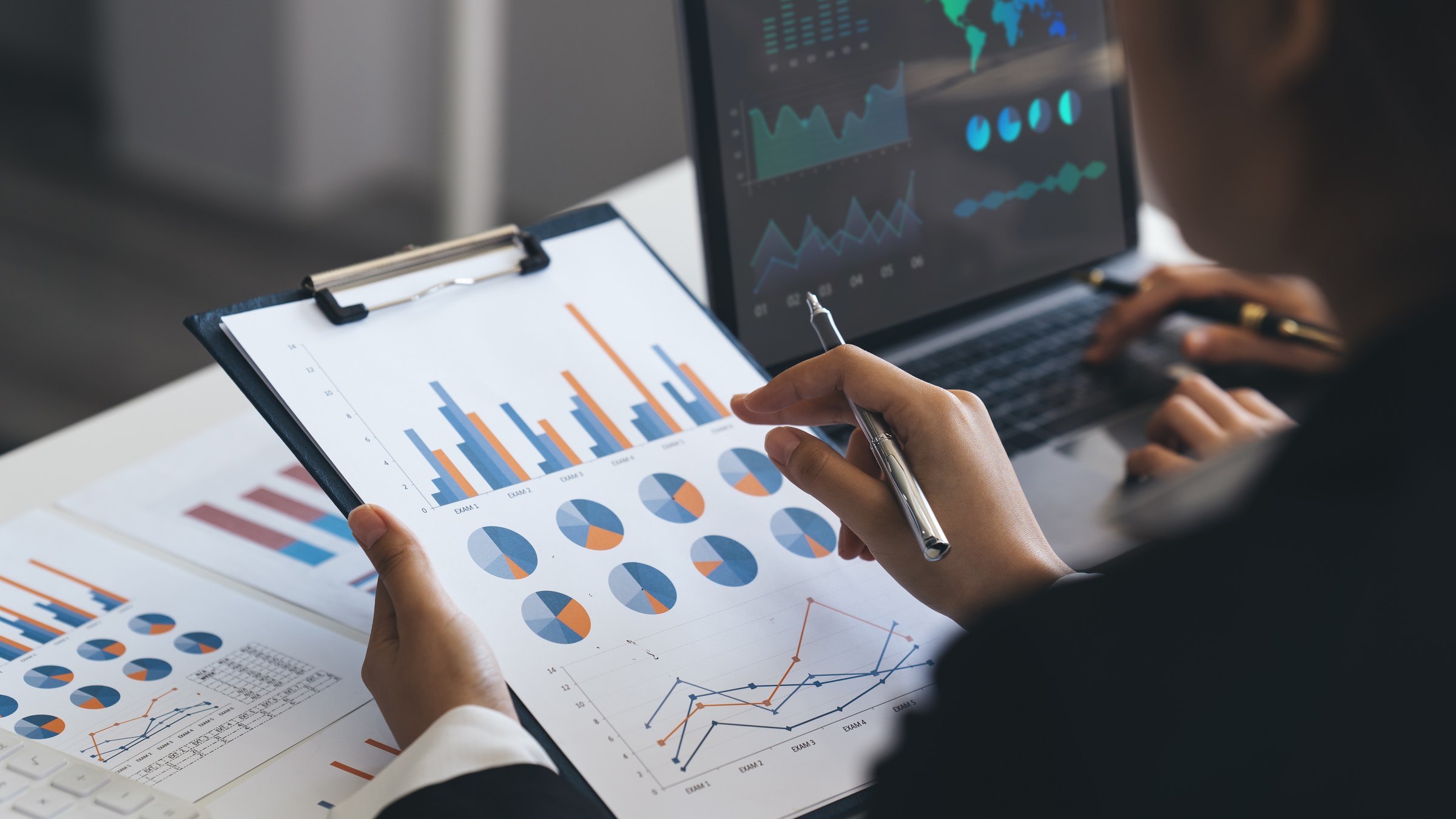 Analyst comparing spreadsheet charts on paper and laptop